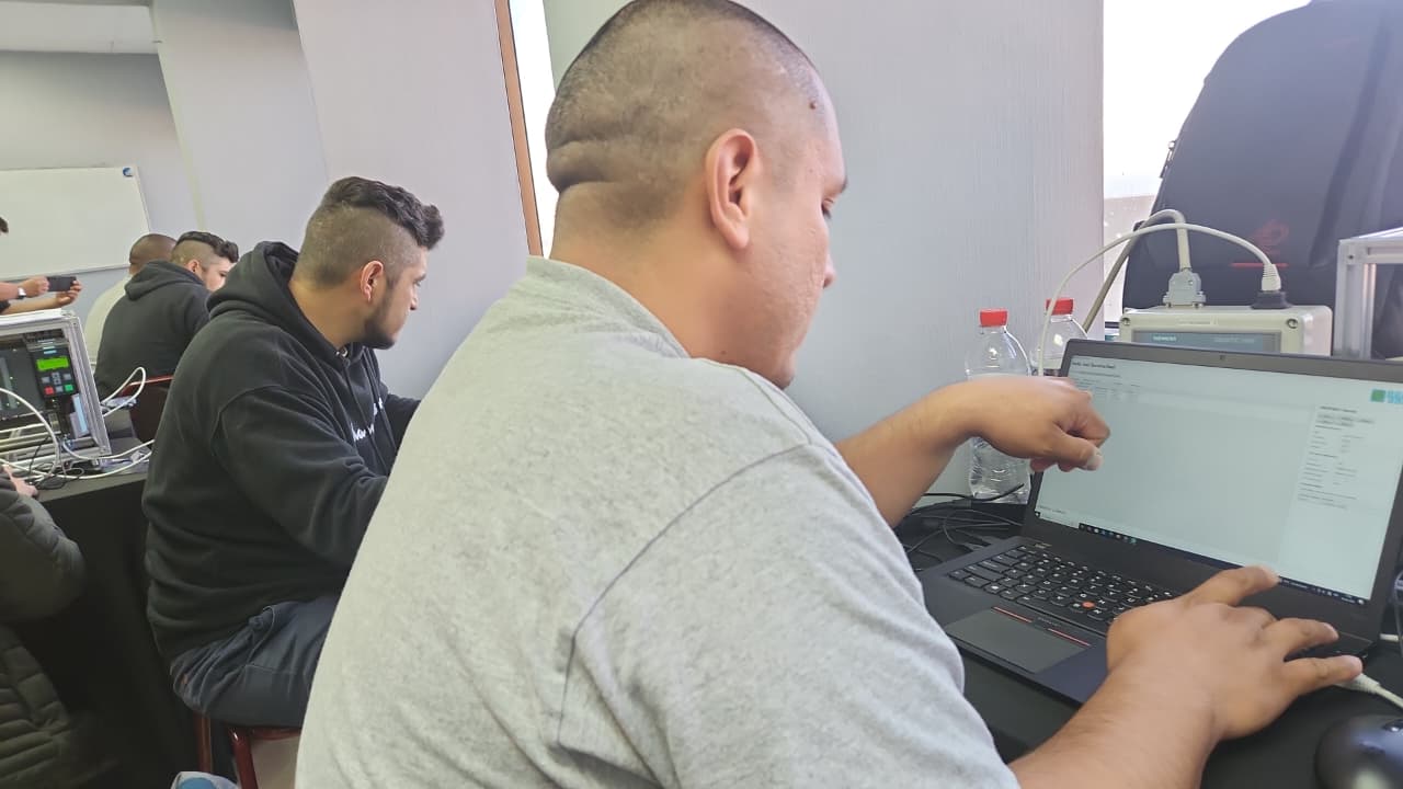 Participantes del curso trabajando en sus notebooks durante una jornada, con el panel SIMATIC al fondo