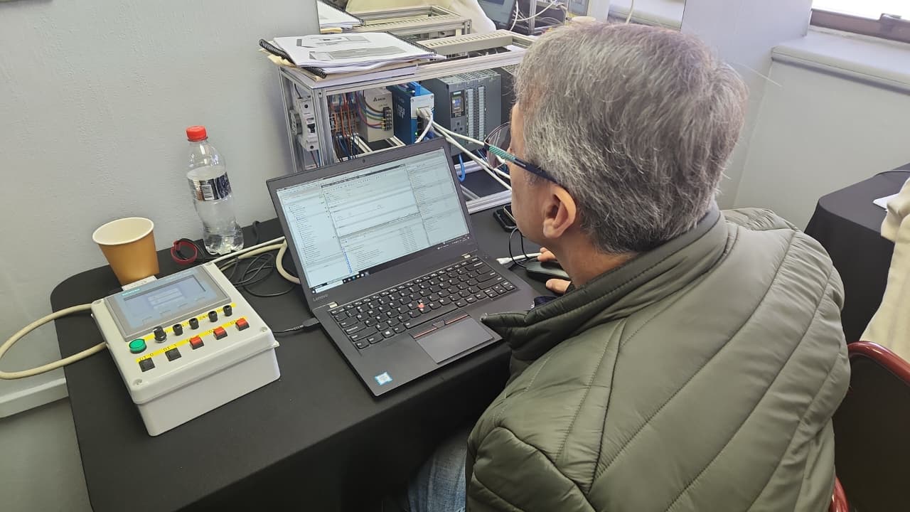 Participante programando en TIA Portal junto al tablero de simulación con pulsadores y luces piloto
