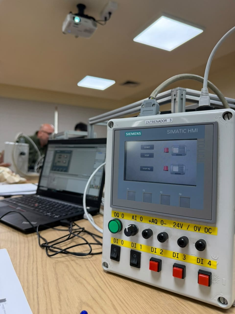 Entrenador con panel SIMATIC HMI que muestra el arranque y la parada de dos motores, junto a sus pulsadores, potenciómetro y bornes de prueba