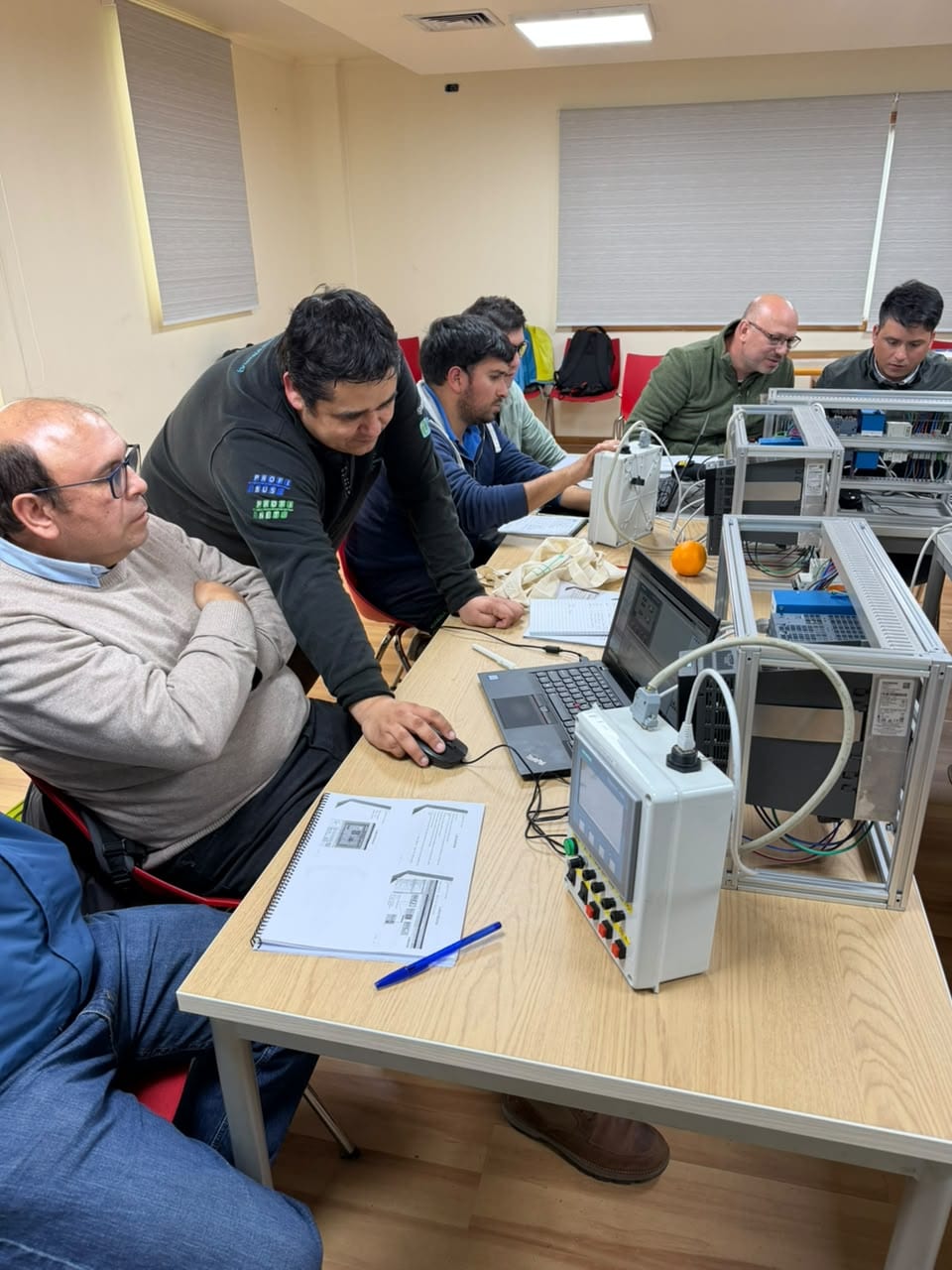 Relator de ControlSIM acompañando a un participante en la estación con el panel SIMATIC HMI y la botonera del entrenador
